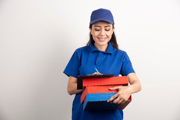 Mensajero mujer escribiendo en portapapeles y sosteniendo cartones de pizza