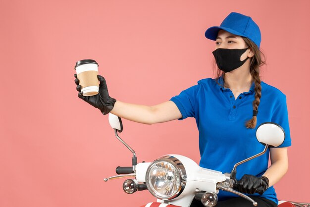 Mensajero mujer feliz vistiendo guantes y máscara médica negra entregando pedidos sobre fondo melocotón