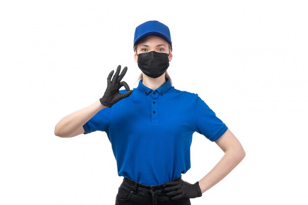 Un mensajero mujer joven de vista frontal en uniforme azul guantes negros y máscara negra posando