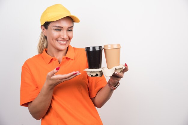 Mensajero mujer rubia apuntando a dos tazas de café en la pared blanca.