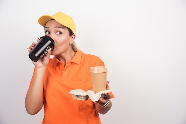 Mensajero mujer rubia bebiendo una taza de café en la pared blanca.