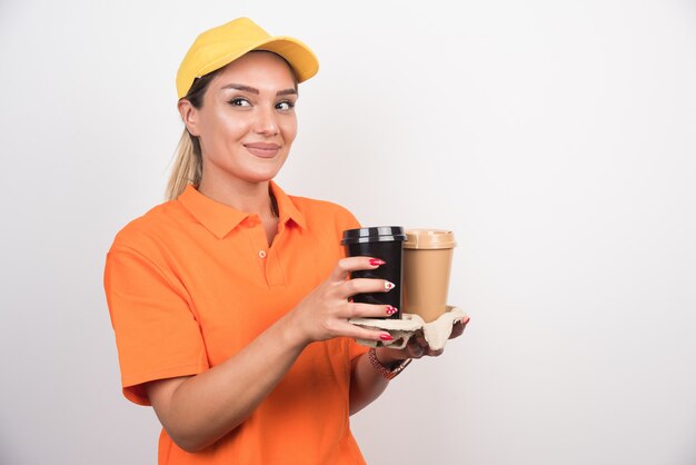 Mensajero mujer rubia mirando a un lado mientras sostiene dos tazas de café.