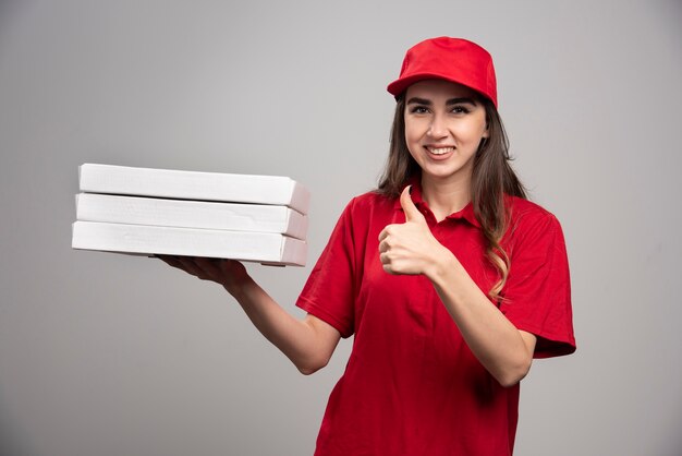 Mensajero mujer sosteniendo cajas de pizza y dando pulgares.