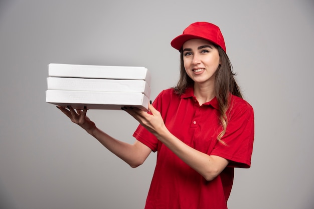 Mensajero mujer sosteniendo cajas de pizza en la pared gris.