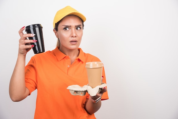 Mensajero mujer sosteniendo dos tazas de café en la pared blanca.