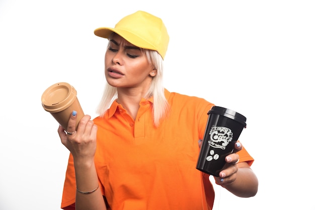 Mensajero mujer sosteniendo y mirando dos tazas de café sobre fondo blanco. Foto de alta calidad