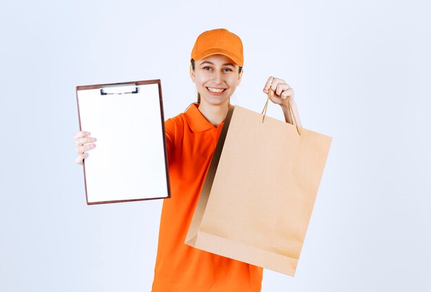 Mensajero mujer en uniforme amarillo entregando una bolsa de compras y presentando la lista de firmas.