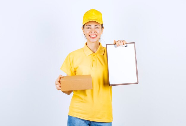 Mensajero mujer en uniforme amarillo entregando el paquete de cartón y pidiendo firmar la lista.