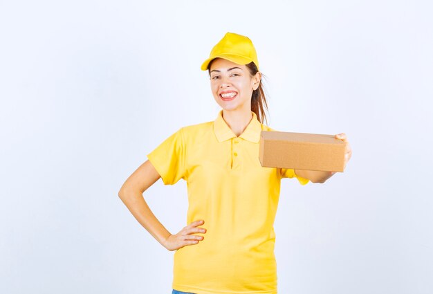 Mensajero mujer en uniforme amarillo entregando un paquete de cartón y sintiéndose positivo.