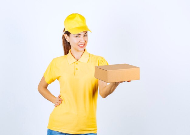 Mensajero mujer en uniforme amarillo entregando un paquete de cartón y sintiéndose positivo.