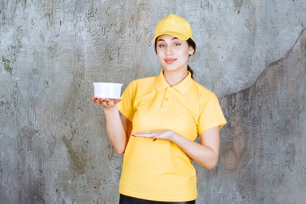 Mensajero mujer en uniforme amarillo sosteniendo una taza de comida para llevar.