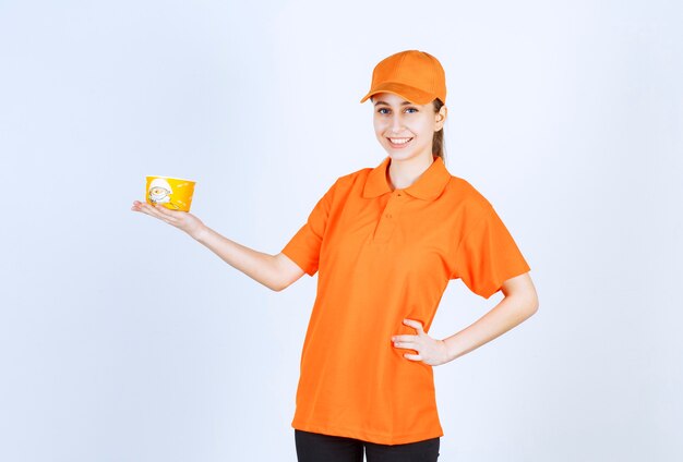 Mensajero mujer en uniforme amarillo sosteniendo una taza de fideos para llevar.