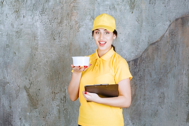 Mensajero mujer en uniforme amarillo sosteniendo una taza para llevar y una carpeta negra.