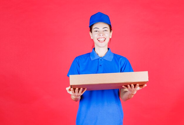 Mensajero mujer en uniforme azul sosteniendo una caja de cartón de pizza para llevar.