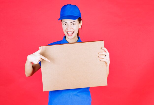 Mensajero mujer en uniforme azul sosteniendo una caja de cartón de pizza para llevar.