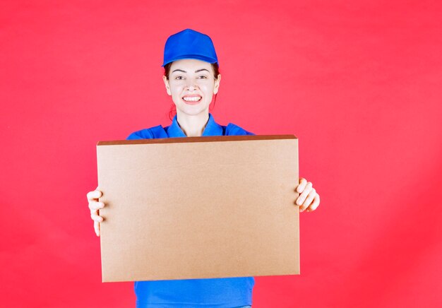 Mensajero mujer en uniforme azul sosteniendo una caja de cartón de pizza para llevar.