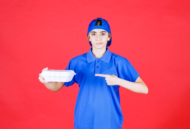 Mensajero mujer en uniforme azul sosteniendo una caja de comida para llevar blanca.