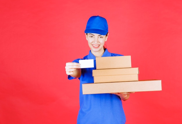 Mensajero mujer en uniforme azul sosteniendo un stock de cajas de cartón y presentando su tarjeta de visita.