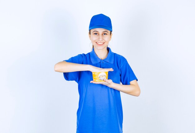 Mensajero mujer en uniforme azul sosteniendo una taza de fideos para llevar.