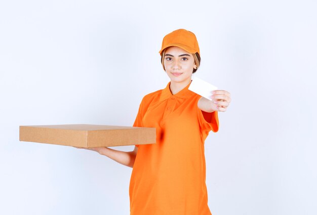 Mensajero mujer en uniforme naranja sosteniendo una caja de cartón y presentando su tarjeta de visita