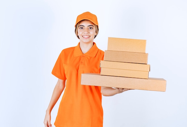 Mensajero mujer en uniforme naranja sosteniendo un stock de paquetes de cartón