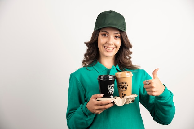 Mensajero mujer en uniforme sosteniendo café para llevar y dando pulgar hacia arriba.