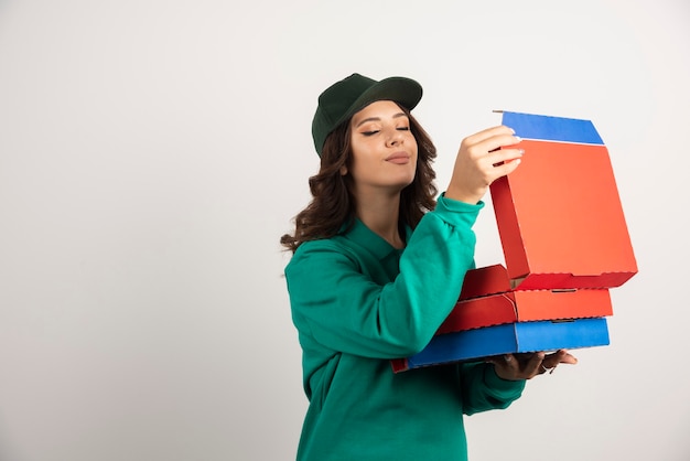 Mensajero mujer en uniforme verde oliendo la pizza caliente.