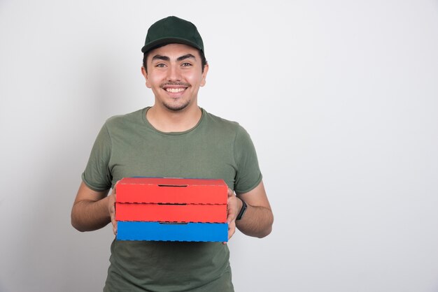 Mensajero positivo sosteniendo tres cajas de pizza sobre fondo blanco.