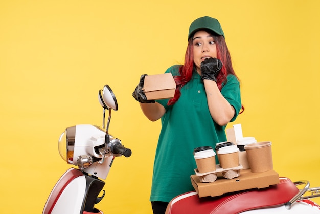 Mensajero de sexo femenino joven con entrega de café en amarillo