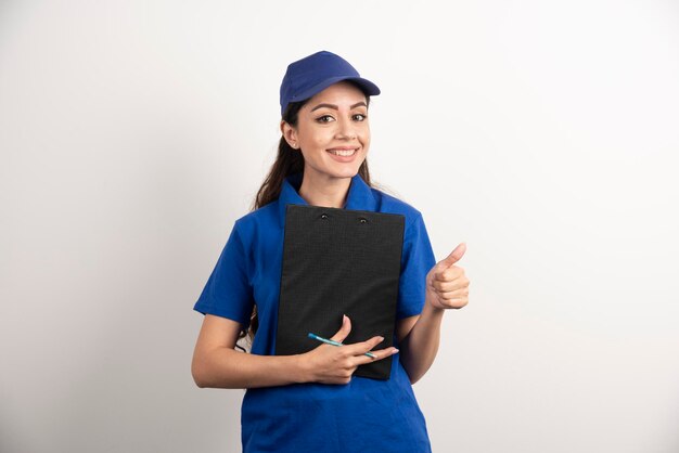 Mensajero de sexo femenino joven en matorrales azules que sostienen un portapapeles. Foto de alta calidad