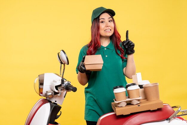 Mensajero de sexo femenino joven con el paquete de comida y café de entrega en amarillo