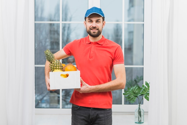 Foto gratuita mensajero sonriente con caja de frutas