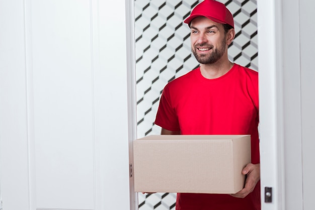 Foto gratuita mensajero sonriente sosteniendo una caja pesada