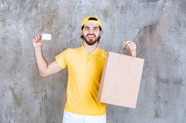 Mensajero en uniforme amarillo sosteniendo una bolsa de cartón y presentando su tarjeta de visita