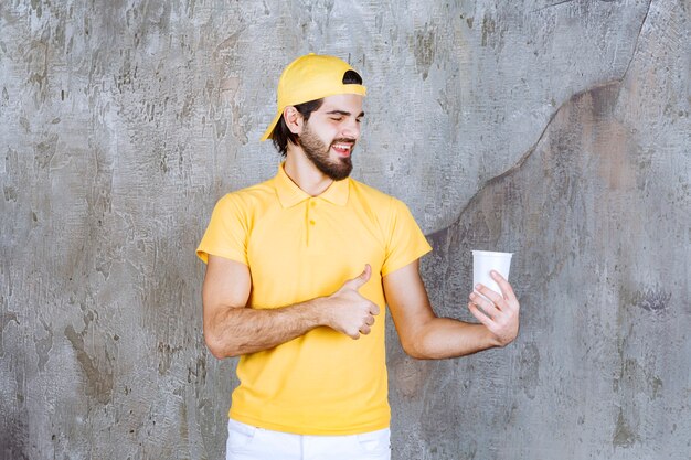 Mensajero en uniforme amarillo sosteniendo un vaso desechable y mostrando un signo de mano positivo.