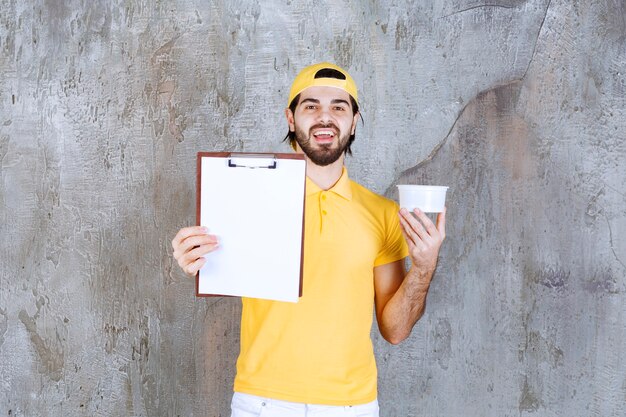 Mensajero con uniforme amarillo sosteniendo un vaso de plástico y pidiendo una firma.