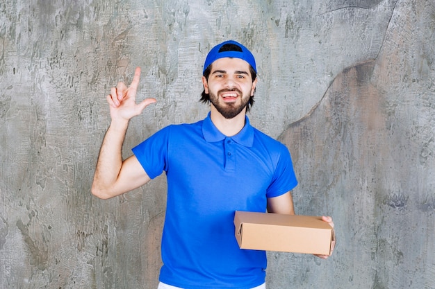 Mensajero con uniforme azul sosteniendo una caja de comida para llevar y parece confundido o tener una nueva idea.