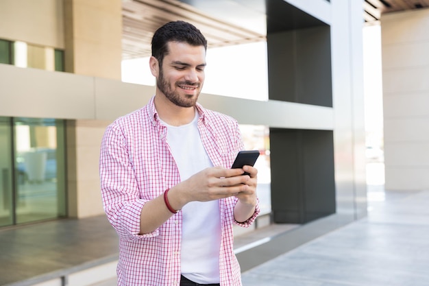 Mensajes de blogger joven sonriente en el teléfono móvil en el centro comercial