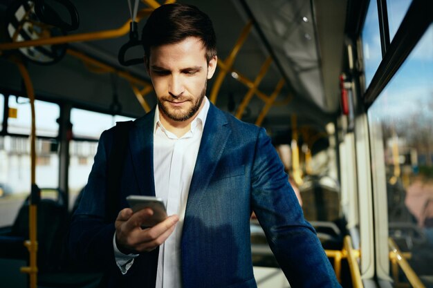 Mensajes de texto de empresario en el teléfono móvil mientras viaja al trabajo en autobús público