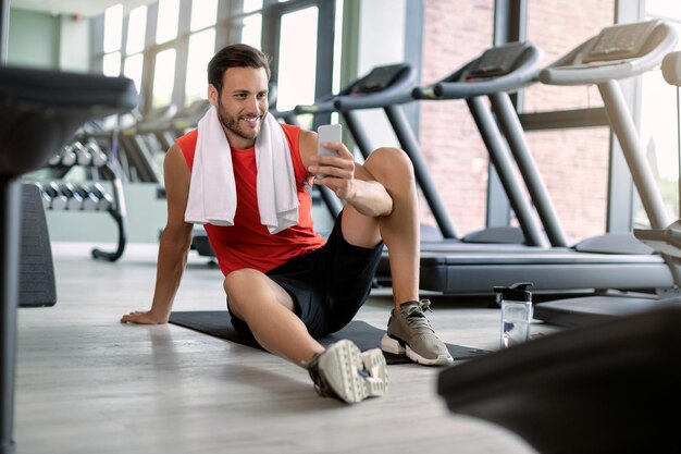 Mensajes de texto de hombre atlético feliz en el teléfono celular en el club de salud