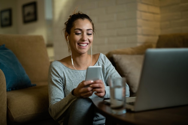 Mensajes de texto de mujer feliz en el teléfono celular mientras se relaja en la sala de estar