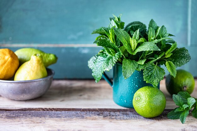 Menta orgánica fresca y bálsamo de limón en una taza de metal, y limas y limones en una mesa de madera. Copia espacio