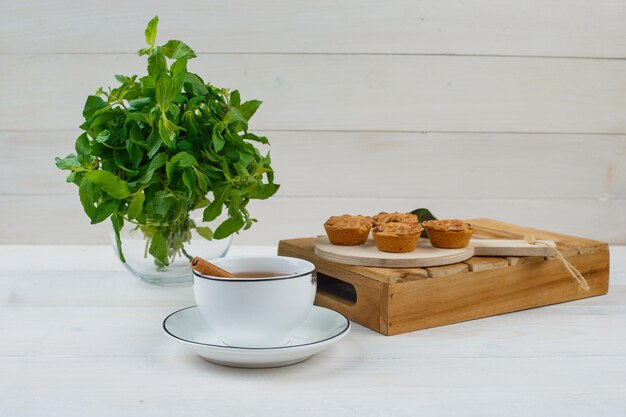 Menta en un tarro de albañil con una taza de té, tortas en la tabla de cortar