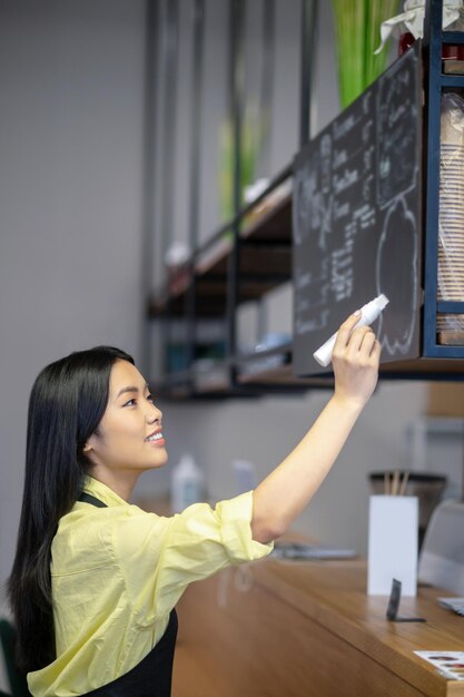 Menú. Mujer joven asiática escribiendo menú en un tablero en un café