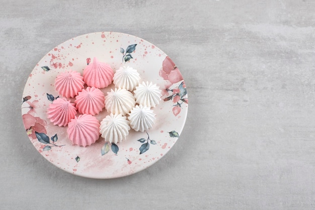 Merengue rosa y blanco en un plato, sobre la mesa de mármol.