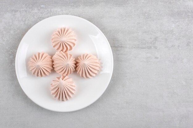 Merengue rosa en un plato, sobre la mesa de mármol.