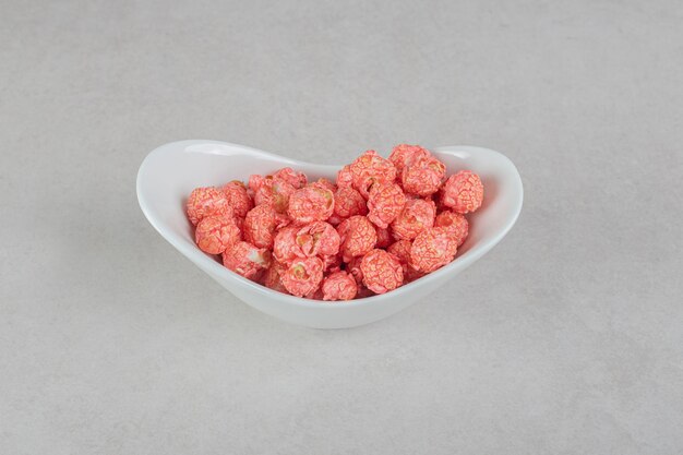 Merienda que sirve de caramelo de palomitas de maíz rojo en un recipiente ovalado sobre mesa de mármol.