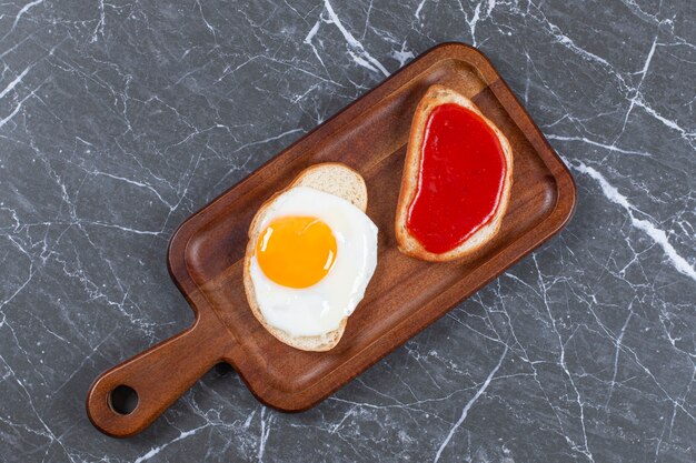 Mermelada y huevos fritos en dos rebanadas de pan en el tablero, sobre la superficie de mármol