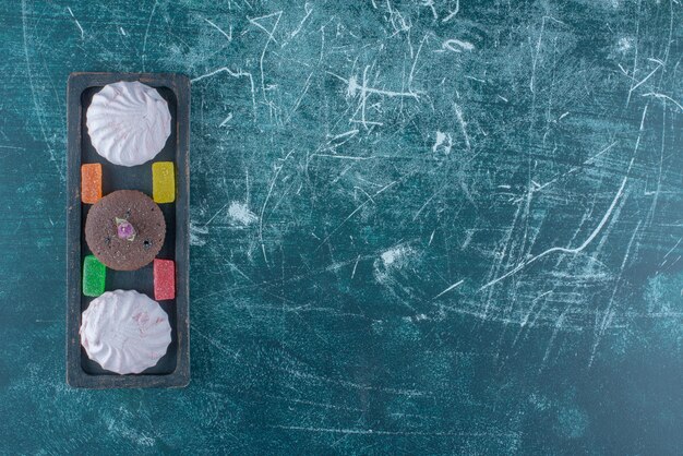 Mermeladas, galletas y un cupcake de chocolate en una pequeña bandeja sobre fondo azul. Foto de alta calidad