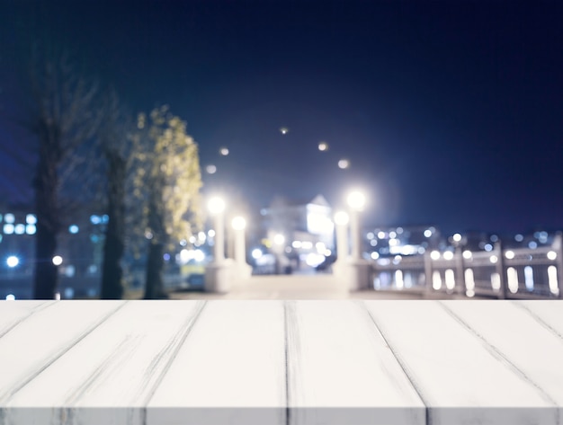 Mesa blanca de madera vacía frente a luces de la ciudad borrosa en la noche